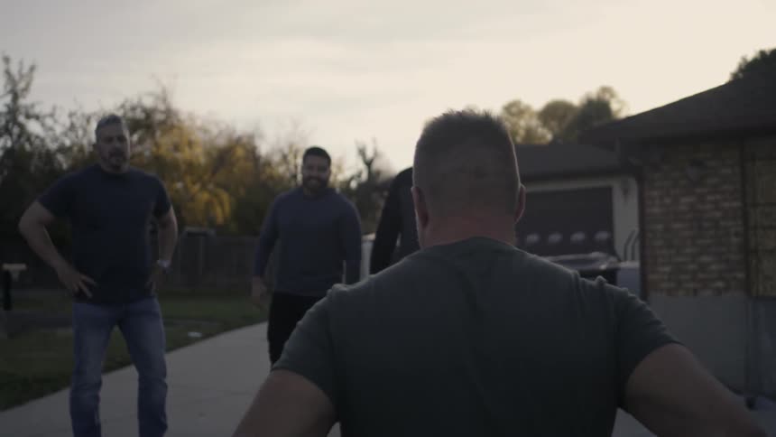 A man in a wheelchair wheels up a driveway to a group of men