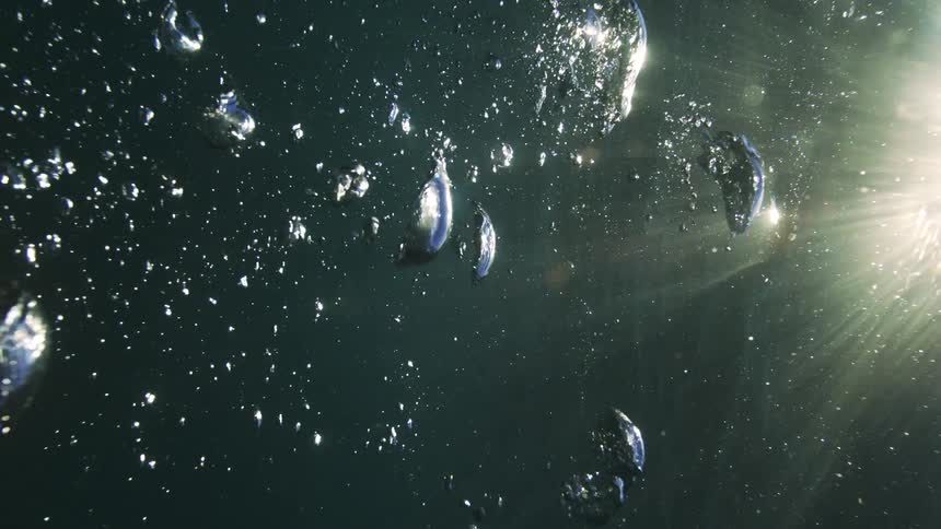 Ethereal underwater shot of air bubbles rising in slow motion with bright sunlight shining through the surface