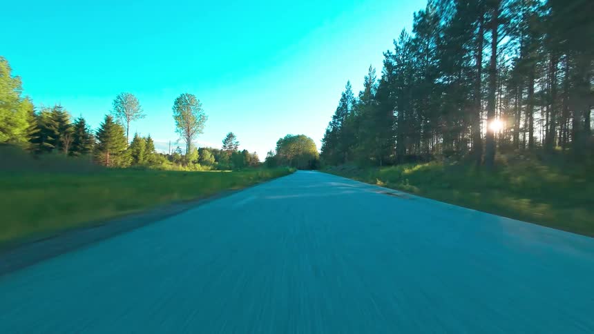 An exhilarating low-angle FPV drive along a rural road, with the golden hour sun shining through a dense forest