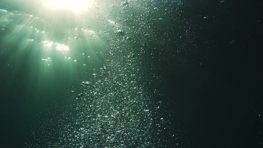 Sun rays filter through the ocean surface as air bubbles rise from the deep