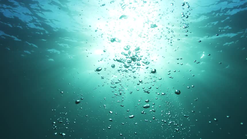 Underwater view of air bubbles rising to the sunlit surface of the turquoise ocean in slow motion