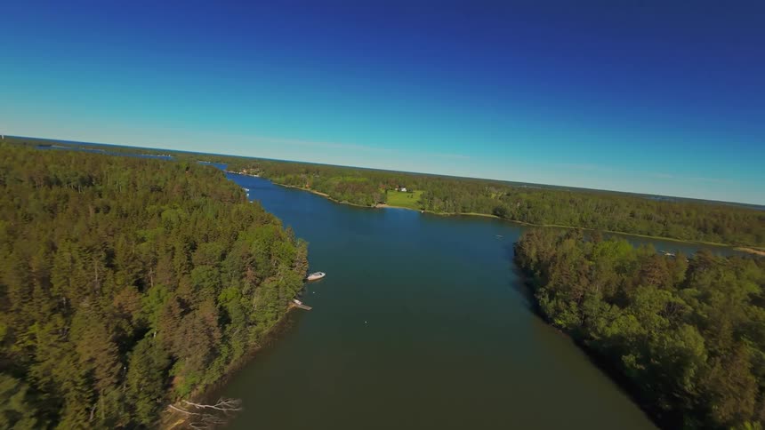 An exhilarating FPV drone flight soaring over a tranquil river winding through a lush green forest under a clear blue sky