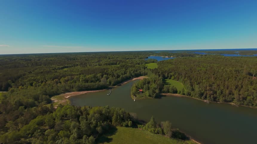 An expansive aerial flight over a lush green landscape of forests and winding rivers on a beautiful, clear sunny day