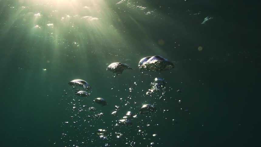 Ethereal slow motion shot of air bubbles rising through deep water with beautiful sun rays piercing the surface