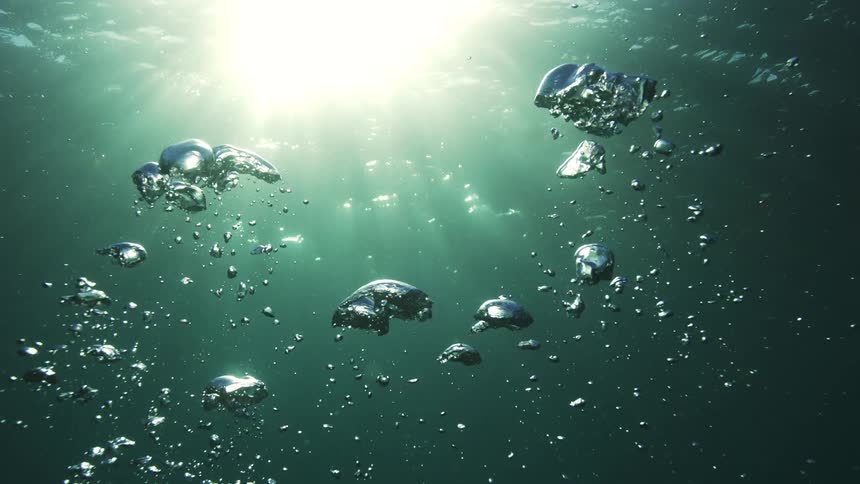 Ethereal slow-motion shot of air bubbles gracefully rising through deep green water towards the sunlit surface