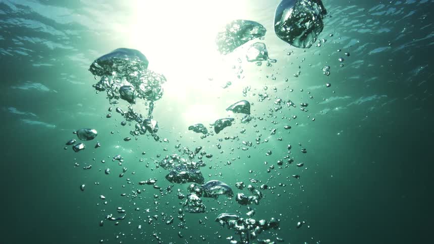 Slow-motion view of air bubbles rising through deep green water towards the sunlight at the surface