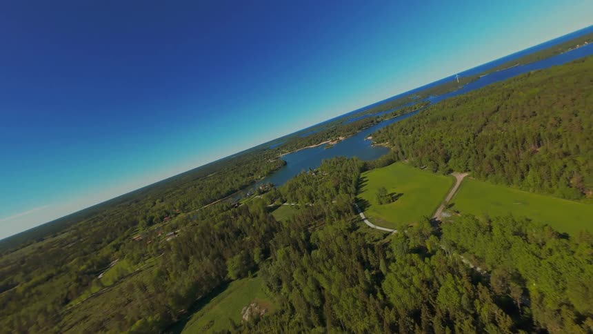 Dynamic aerial footage soaring over a vast, green forest landscape dotted with lakes under a brilliant blue sky