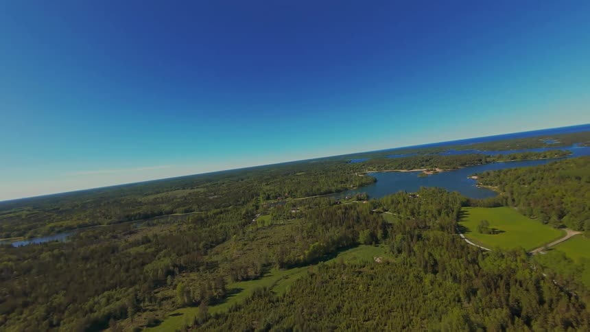 A sweeping aerial view pans and levels out to reveal a vast Scandinavian archipelago landscape of lush forests and lakes on a clear day