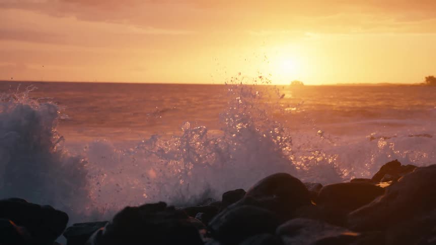 Golden hour sunset illuminates ocean waves as they crash against the rocks in breathtaking slow motion