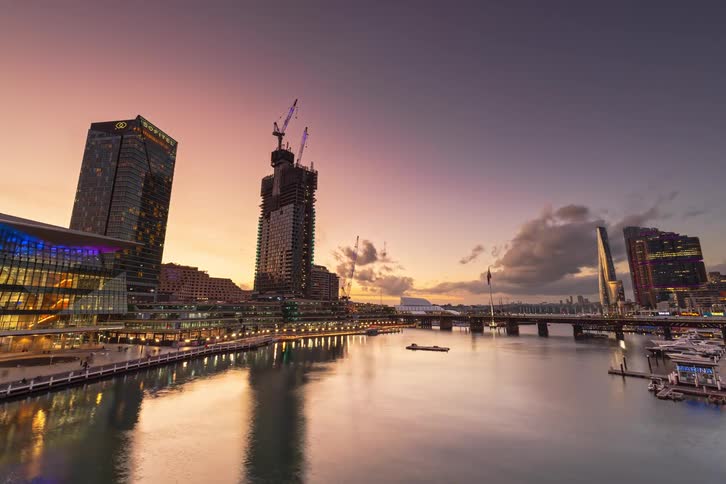 A stunning day-to-night timelapse of Sydney's Darling Harbour, where the warm sunset gives way to a vibrant cityscape with colorful lights reflecting on the water