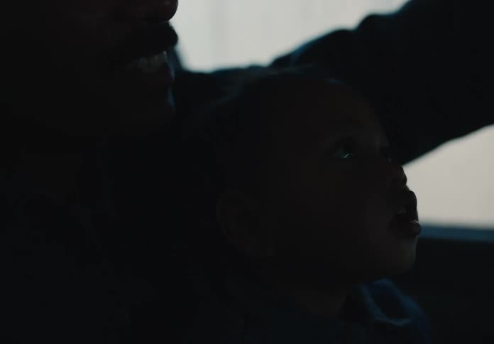 A toddler looks up in wonder from his father's lap as they drive through a dark tunnel