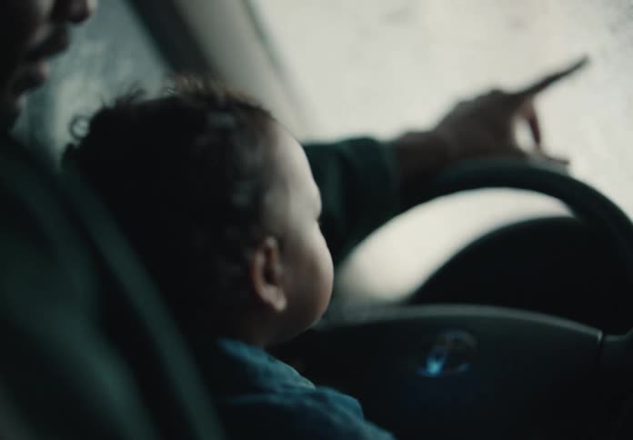 A curious baby sits on their parent's lap and watches the water and soap slide down the windshield in a car wash