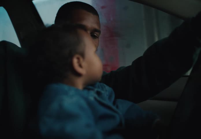 A smiling father holds his young son on his lap as they look up in wonder while driving through a car wash