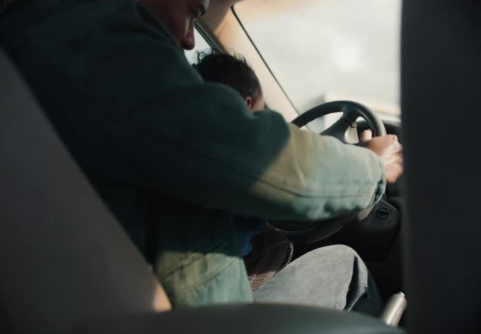 A loving father holds his baby on his lap while sitting in the driver's seat of their car, sharing a tender moment together