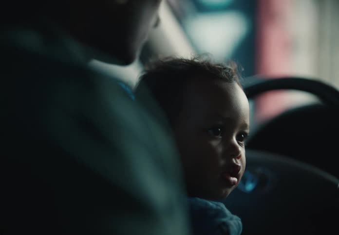 Close-up of an adorable toddler looking over their shoulder while sitting inside a dimly lit car