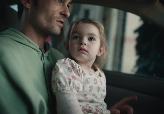 A father holds his curious young daughter on his lap as they watch the automatic car wash together from inside their vehicle