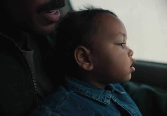 A curious toddler looks out the car window with wide-eyed wonder while sitting on their father's lap