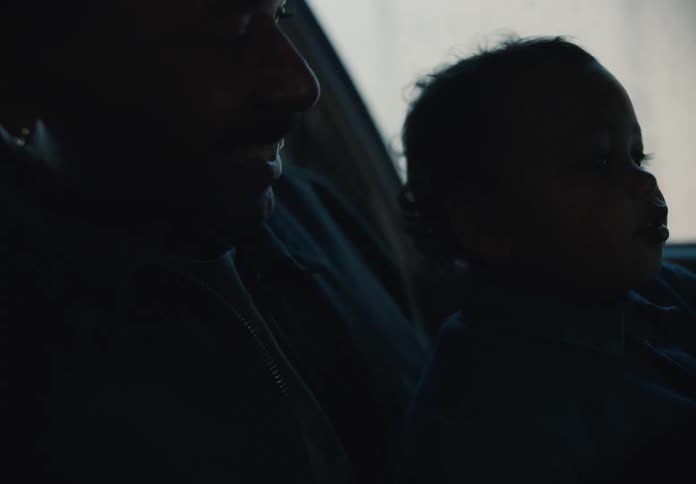 A young child sits on their father's lap, looking out the car window with wonder as they share a tender moment together on a drive