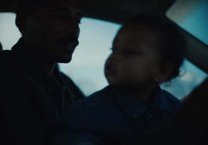 Candid moment of a father driving his car while holding his curious toddler on his lap at dusk