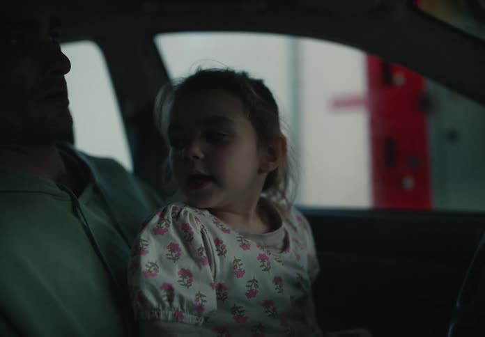 Close-up of a curious toddler girl sitting on her father's lap in the car, watching something with wide eyes