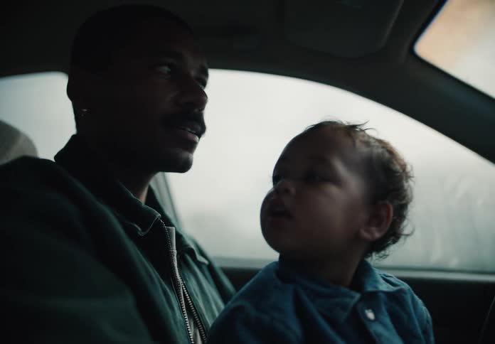 A loving African American father holds his curious toddler on his lap while driving and talking to them during a car ride