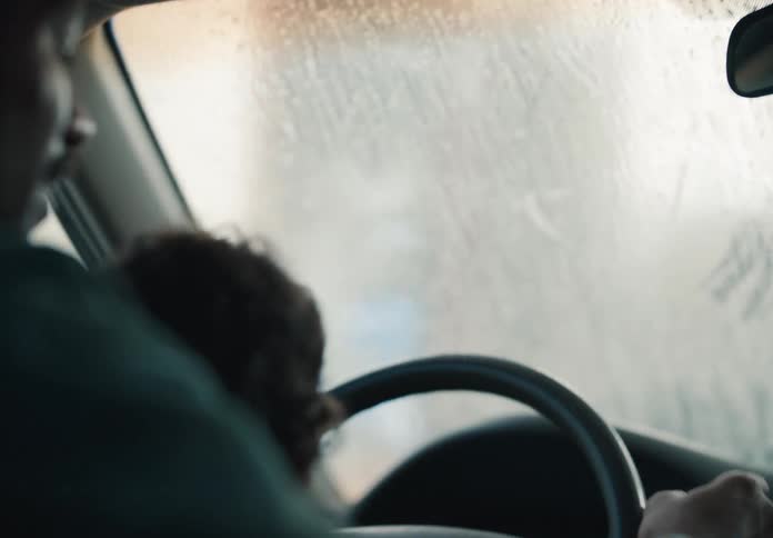 A curious baby boy sits in his father's lap and plays with the steering wheel while they go through a car wash