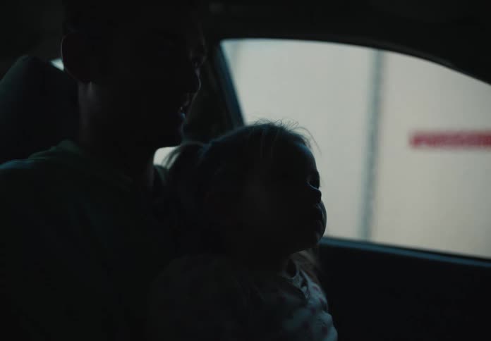 A mesmerized little girl sits on her father's lap, watching intently as they go through a car wash