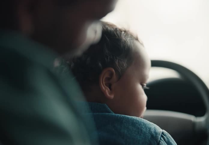 An adorable baby sitting in a car scrunches up its nose and smiles after a parent playfully boops it