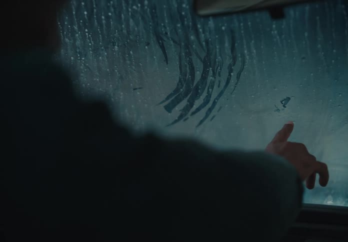 A tender moment as a father and his child draw on the condensation of a car window during a rainstorm