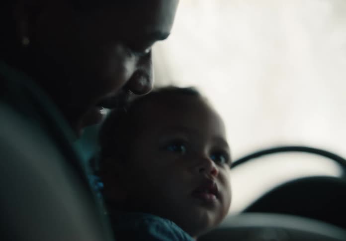 A loving father smiles while driving with his curious young child sitting on his lap