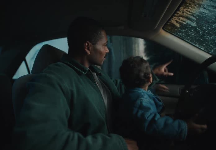 A loving father holds his curious toddler on his lap as they go through an exciting car wash at night