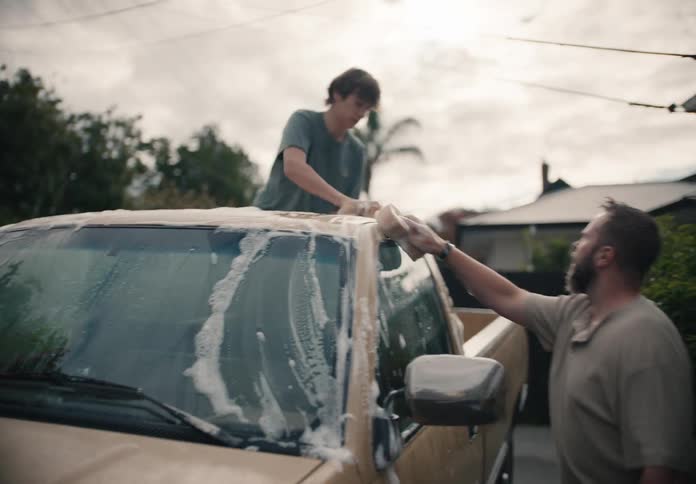 Father and son bond while washing their tan pickup truck together in the driveway