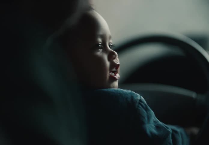 Over-the-shoulder close-up of a cute toddler pretending to drive in a softly lit car