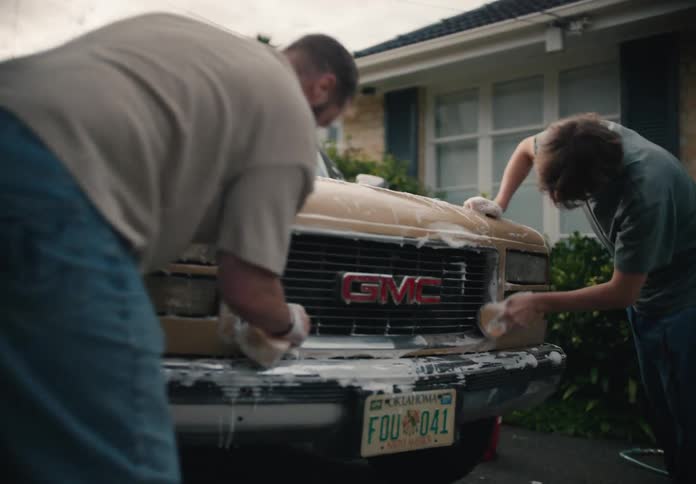 A father and his teenage son wash their pickup truck together in the driveway of their home