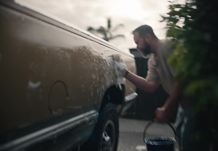 Slow motion footage shows a father and son washing their old, sudsy pickup truck together in the driveway of their home