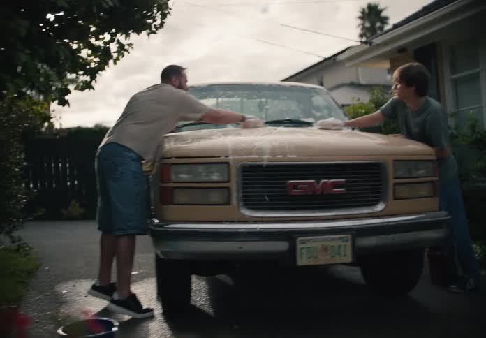 A father and son wash their pickup truck together in the driveway of their suburban home