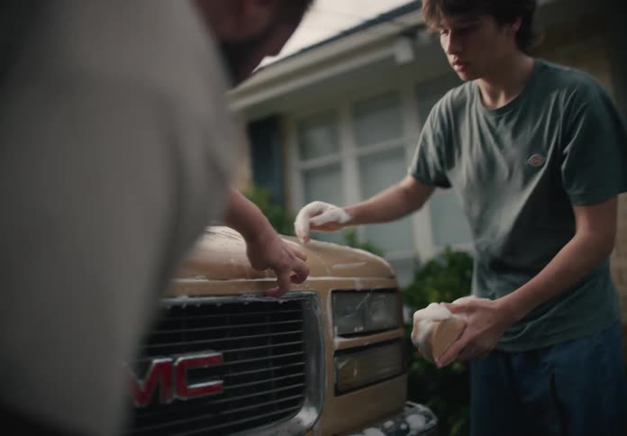 A father and his son bond while washing a vintage pickup truck together in the driveway of their home