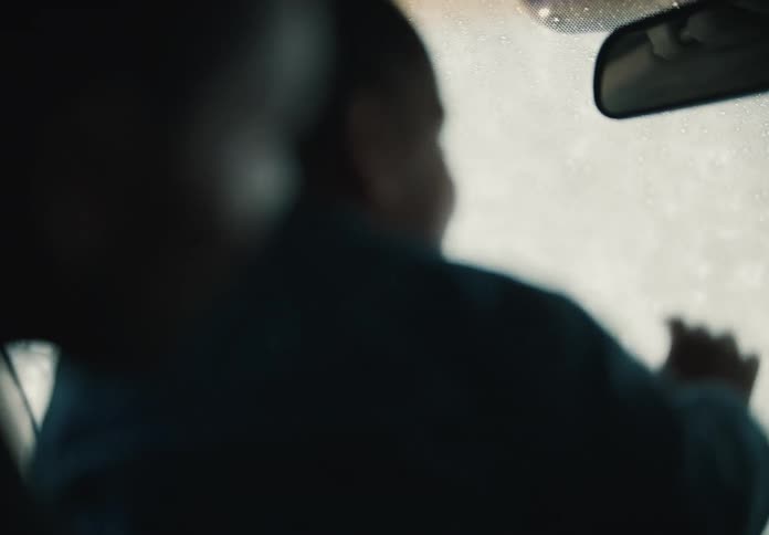 An out-of-focus toddler curiously touches the wet windshield from inside a car