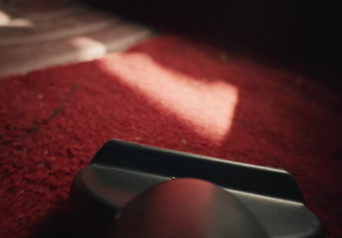 An extreme close-up of a vacuum cleaner nozzle sucking up dust from a red carpet in slow motion