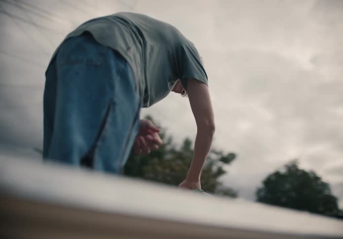 From a low angle, a young man stands in the bed of an old pickup truck and washes it out with a garden hose on a cloudy day