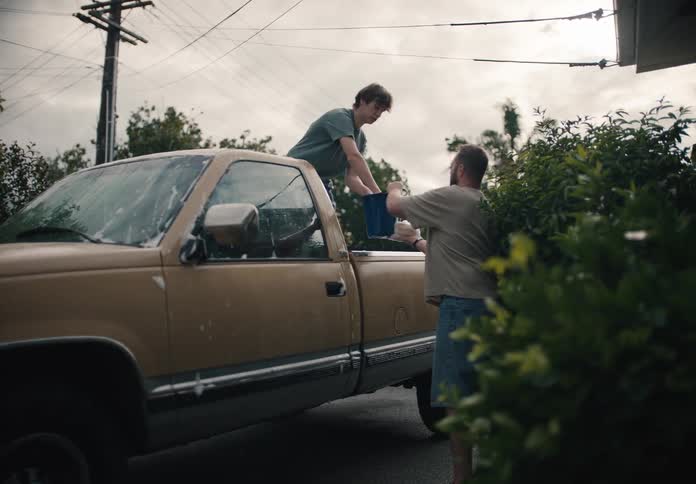 A father and his teenage son spend quality time together washing their old pickup truck in the driveway in slow motion
