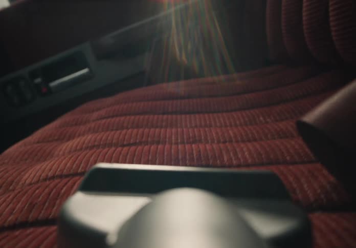 A close-up, point-of-view shot of a vacuum cleaner cleaning a vintage red car seat