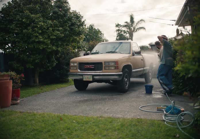 A father teaches his son how to use a power washer to clean their pickup truck in the driveway of their suburban home