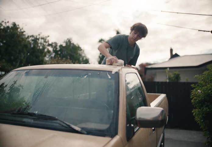 A father and his teenage son work together to wash their pickup truck in the driveway of their home in slow motion