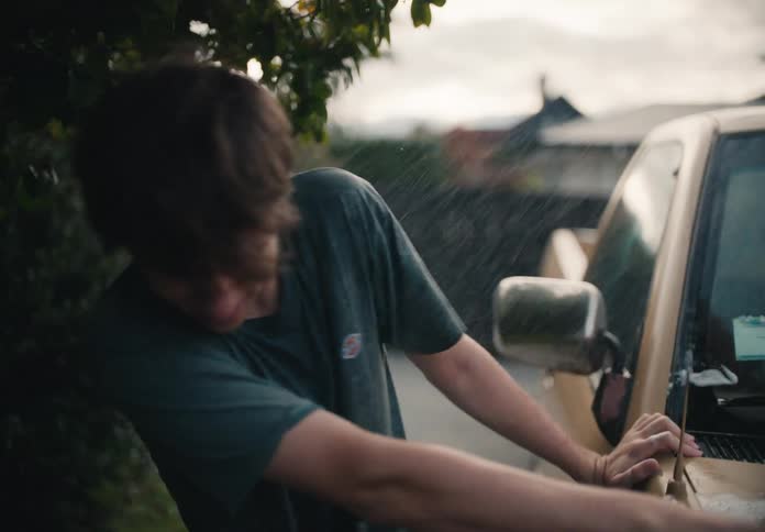 A smiling young man washes a car in slow motion in a suburban driveway