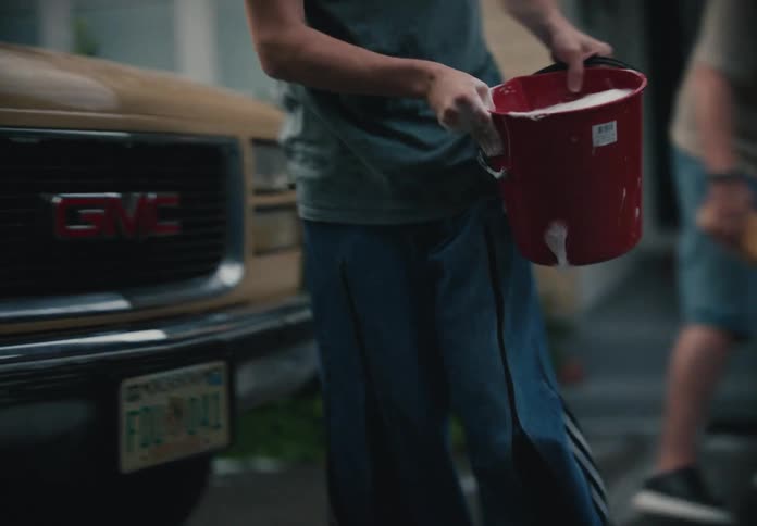 Father and son fill a red bucket with soapy water in slow motion, preparing to wash their vintage pickup truck