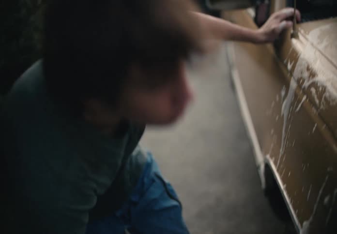 A young man diligently washes a truck with a soapy sponge in a suburban driveway in slow motion