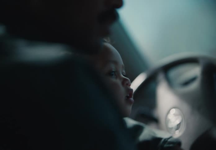 A soft-focus close-up shows an adorable toddler sitting beside their father during a peaceful car ride
