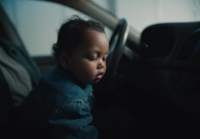 A sleepy toddler dozes off while sitting on his father's lap behind the steering wheel