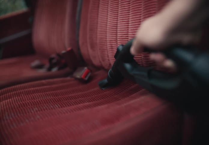 Detailing an old car's interior by vacuuming the red cloth bench seat